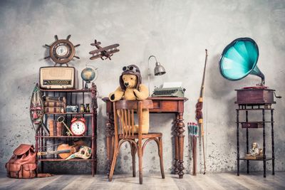 Vintage collectibles staged for auction — gramophone, typewriter, radio, globe and a teddy bear at a writing desk